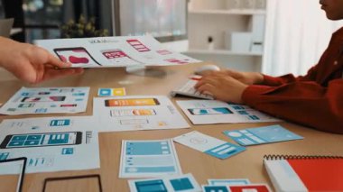 Mobil uygulama için kullanıcı arayüzü prototipini ofis çalışanlarına sunan harika bir şirket çalışanı. UX UI tasarımcısı kağıt üzerinde simge tasarımının işlevini açıklıyor. Sinerjik