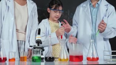 Liseli kız renkli çözeltileri karıştırırken akademik öğrenci desteği de mikroskop ve sıvıyla deney yapıyor. Tahtada bilim teorisi yazılı çeşitli öğrenciler var. Öğretim