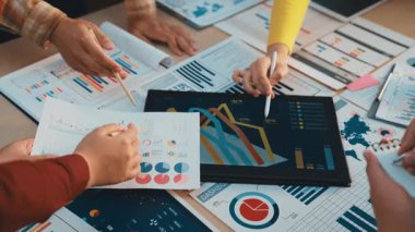 Çeşitli profesyonellerden oluşan bir grup, bir dizüstü bilgisayarda sergilenen veri ve çizelgeleri analiz ederek stratejik planlama ve takım çalışmasını teşvik ederek, işbirlikçi bir iş toplantısına katıldı. SACTR