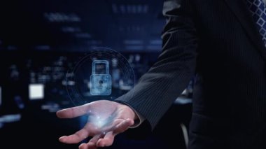 Modern bir iş ortamında gelişmiş siber güvenlik ve yenilikçi teknolojiyi sembolize eden, veri görselleriyle çevrili dijital bir kilit sunan profesyonel bir el. Dörtgen