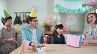 Çekici beyaz kız, ebeveynleri kutlama yaparken ve parti şapkası takarken doğum günü hediyesi alıyor. Mutlu genç çocuk gülümserken mutlu aile özel günü kutlamak için el çırpıyor. Pedagoji