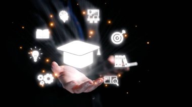 Eğitim ve yenilik sembolleriyle çevrili mezuniyet şapkası amblemini tutan bir elin dinamik görüntüsü bilginin ve başarının önemini gösteriyor. Dörtgen