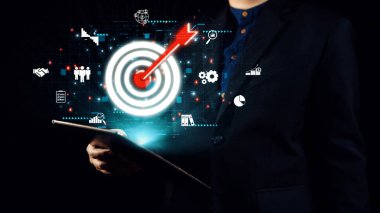 Bir iş adamı, dijital ikonlar ve modern bir ortamda pazarlamayı ve stratejik başarıyı sembolize eden bir hedefle çevrili bir tableti güvenle elinde tutuyor. Dörtgen