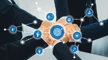 Odaklanmış bir iş ekibi, yenilik ve başarıyı temsil eden hedef simgelerin dijital arayüzü ile geliştirilen işbirliği ve hedefe ulaşmayı sembolize etmek için el ele veriyor. Dostluk