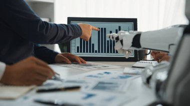 Bir iş ekibi, robotsal teknolojinin de yardımıyla, trendler ve stratejik planlama üzerine odaklanarak, ekranda sunulan verileri analiz ederek, modern bir ofis ortamında işbirliği yapmaktadır.