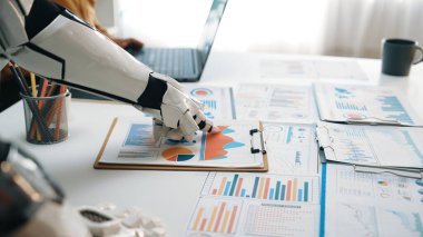 Robotik bir el modern bir ofisteki bir panoda iş haritalarını ve grafikleri yakından inceler. Sahne teknolojinin veri analizi ve takım çalışmasındaki rolünü vurguluyor. Noogenesis