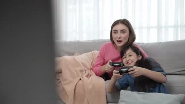 Annem kanepede yatarken, mutlu kız oyun oynuyor ve oturuyor. Beyaz bir ebeveyn ve çekici zeki bir kız elinde joystick ile birlikte vakit geçirip maç kazanmaya odaklanıyor. Yaşam tarzı. Pedagoji.