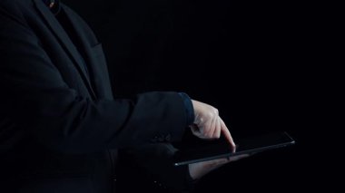 Bir işadamı, mali büyümenin görsel temsili, yükselen eğilimleri ve karanlık bir arkaplana karşı veri analizini vurgulayan dijital bir tablet sergiliyor. Dörtgen