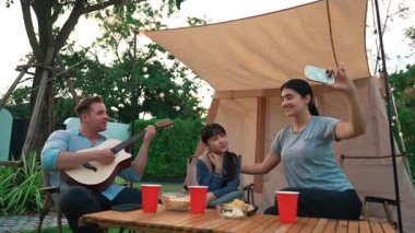 Baba gitar çalarken anne ve kızı bahçede kamp yapıyor. Ebeveynler, genç nesil çapraz kuşak farklılıklarıyla zaman geçirmek için açık hava kamp aktivitelerini kullanıyorlar. Uyumsuzluk.