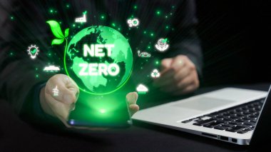 Modern teknolojide sürdürülebilirlik ve çevresel sorumluluğun önemini vurgulayan akıllı telefon ve dizüstü bilgisayarla net sıfır kavramını gösteren profesyonel bir ortam. Dörtgen