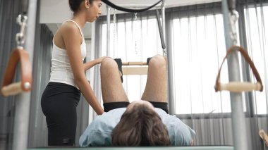 Cadillac ekipmanları üzerinde bacak kaldırma egzersizinde müşteriye yardımcı olan yetenekli pilates eğitmeni. Kadın antrenör, Cadillac 'ın bacak gerdirme hareketine yardım ediyor. Temel bağlantıyı geliştirmek için, bacak esnekliği için. Alışkanlık.