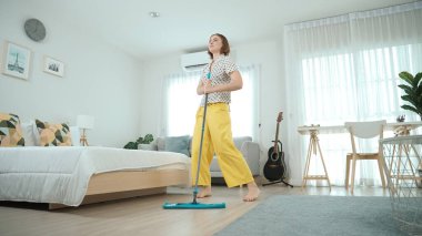 Modern apartman dairesinde dans ederken yerleri paspaslayan beyaz bir hizmetçi. Mutlu enerjik anne ya da temizlikçi müzik eşliğinde oturma odasını temizlemekten zevk alır. Yaşam tarzı. Pedagoji.