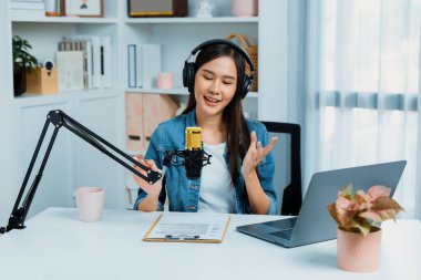 Sosyal medyada kulaklıkla canlı yayın yapan Asyalı sunucu modern stüdyoda yaşam koçluğu veya pazarlama dinleyicilerini selamlıyor. Taktik.