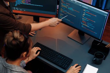 Akıllı web sitesi geliştirme kodlayıcı sistemi ile tartışan IT geliştiricilerinin üst görüşü modern ofisteki neon ışık odasında iki ekran bilgi teknolojisini çevrimiçi çalıştırıyor. İnfobahn.