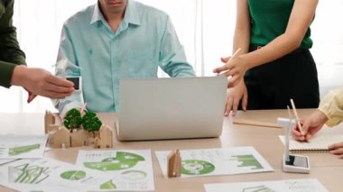 Yel değirmeni modeline ve ev şeklindeki bloğa danışmanlık yapan işadamları, Dünya Yöneticisi 'nin dizüstü bilgisayar üzerinde çalışmasını kurtarmak için yeşil enerji kullanımına referans olarak başvuruyorlar. Tanımlama.