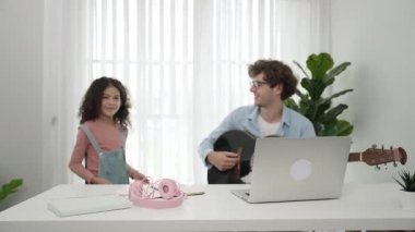 Çekici beyaz bir baba gitar çalarken tatlı bir kız müzik eşliğinde dans ediyor. Mutlu baba ve Amerikalı kız birlikte vakit geçirirken akıllı çocuk müzik yapıyor. Aile eğlence konsepti. Pedagoji.