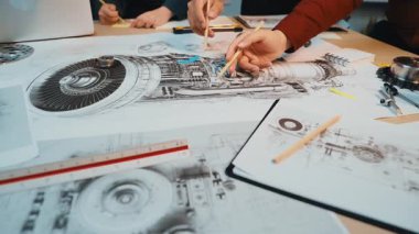 Mekanik tasarımlar ve teknik planlar üzerinde birlikte çalışan mühendisleri yakalayan, yaratıcı bir çalışma alanında yenilik ve takım çalışması sergileyen dinamik bir sahne. SACTR