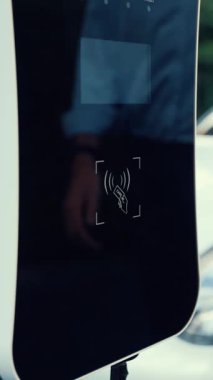 Bir adam kredi kartını, şarj istasyonundaki elektrikli aracının temiz ve sürdürülebilir enerjisini ödemek için kullanıyor. Yenilikçi adam şarj edilebilir aracına güç sağlamak için ödeme yapıyor..