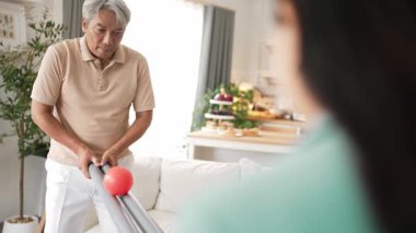 Yaşlı bir adam evde partneriyle top yuvarlama oyunu oynuyor, zihinsel ve fiziksel sağIık için el-göz koordinasyonu, odaklanma ve motor becerileri pratiği yapıyor. Sağlık hizmetleri konseptini engelliyor. Myrmidon.