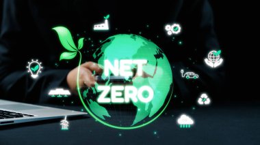 Sürdürülebilir uygulamaları, net sıfır hedefleri ve daha yeşil bir gelecek için yenilikçi teknolojiyi vurgulayan dijital grafiklerle etkileşen modern bir çalışma alanı sahnesi. Dörtgen