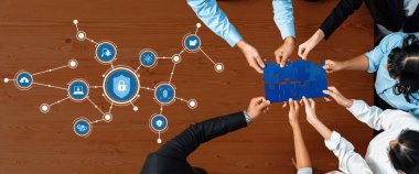 Çeşitli profesyonellerden oluşan bir grup, dijital simgeler üzerinde bir yapboz parçası tutarak, modern bir ofiste takım çalışmasını ve yeniliği sembolize ederek siber güvenlik çözümleri üzerinde işbirliği yapıyor. Dostluk