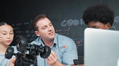 Akıllı öğretmen araba modelini farklı öğrencilere denetliyor. Melez ırk dinleyen liseli çocuklar masada dizüstü bilgisayarı ve kabloları olan robot model sistemini açıklıyor. Öğretim