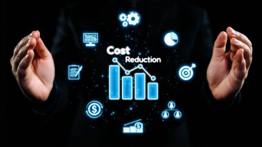 Bir işadamı, parlayan bir grafik ve mali performans ve stratejik planlamayı temsil eden çeşitli simgeleri çevreleyen bir maliyet azaltma kavramını gözler önüne seriyor. Dörtgen