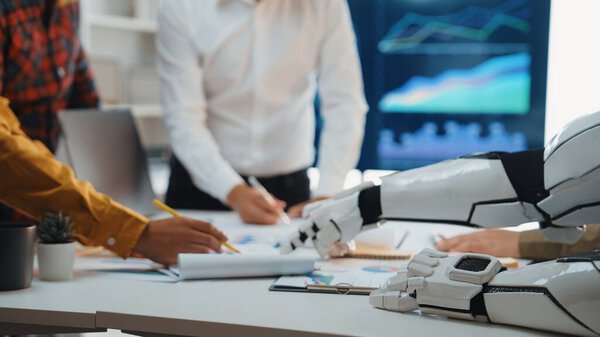 A futuristic office scene showcasing collaboration between human workers and a robotic arm, highlighting innovative technology and data analysis for business growth.Noogenesis