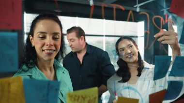 Profesyonel iş adamları, cam duvarda yaratıcı fikirleri paylaşmak için yapışkan notlar kullanarak pazarlama fikrini araştırıyor. Bir grup farklı iş adamları strateji hakkında tartışıyorlar. - Yakın çekim. Yönlendirici.