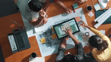 İnşaat mühendislerinin masa başında proje planıyla otururken tablet kullanarak ev yapısını dizayn etmelerine tepeden aşağı bir bakış açısı. Ekip planlama ve inşaat hakkındaki fikirlerin havadan görüşü. Sempozyum.