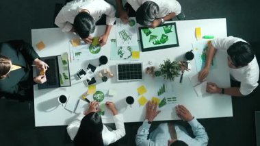 İş adamlarının rüzgar değirmeniyle toplantı masasında temiz enerji ve sürdürülebilir yatırım kullanımı, çevre grafiği ve ahşap ev modeli ile ilgili tartışmalarına tepeden aşağı bakış açısı. Hizalama.