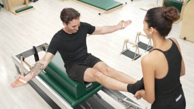 Beden eğitiminde birlikte pilates egzersizi yapan birkaç mutlu antrenör. Çekirdek gücü ve dengeyi arttırmak için reformcuda yüz poz veren İspanyol bir adam. Alışkanlık.