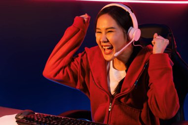 Yüzünde kulaklık renginde kulaklık takan, neon odada online oyun oynayan, Esport meziyetli takım oyuncularına yumruk kaldırarak oynayan güzel Asyalı kız flamasının sunucu kanalı. Taktik.