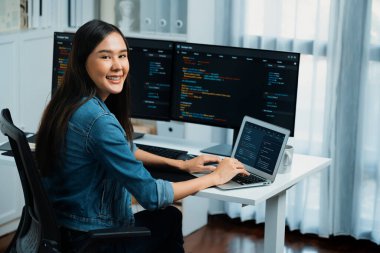 Bilgi teknolojisi geliştirme bölümünden genç bir Asyalı kameraya bakıyor. Kodlama programı veri uygulamalı, kot gömlek giyiyor. Güvenlik analizi ile çevrili iki ekran. Taktik.