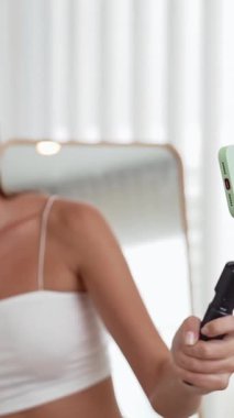 Genç sosyal medyum kadın moda videosu yapıyor. Blogcu kameraya selfie çubuğu ve ışık halkası kullanarak gülümserken, aynı zamanda ikna edici çevrimiçi kıyafetlerin izleyicilere veya takipçilere vlog satmasını sağlıyor. Düzenle