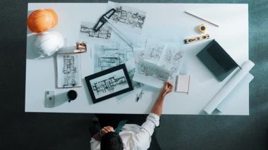 Tablet, dizüstü bilgisayar, güvenlik kaskı ve ekipmanlarla toplantı masasında otururken ev tasarımı için malzeme seçen yetenekli mühendis görüşü. Akıllı mimar proje planına bakıyor. Hizalama.