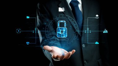 Karanlık bir ortamda duran bir işadamı siber güvenlik ve veri korumasını temsil eden dijital bir kilit sembolü sergiliyor. Görüntü teknolojiyi ve yeniliği ön plana çıkarıyor. Dörtgen