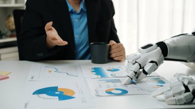 Bir insan ve bir robot, teknoloji ve insan görüşü arasındaki modern işbirliğini gösteren grafikleri ve veri analizlerini tartışmak için bir iş toplantısına katılırlar.