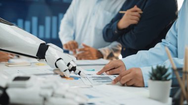 Fütürist bir robot el, iş görüşmesi ortamında verileri analiz eder. Profesyoneller tartışma ve çizelge ve grafiklerle ilgilenir, takım çalışmalarını ve yeniliklerini vurgularlar. Noogenesis