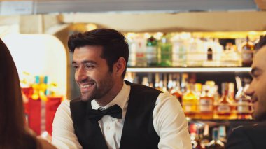 Güzel görünümlü barmen, içki tezgahındaki çiftle samimi bir gülümseme sohbeti yaparken aynı zamanda hoş geldin içkisi ve özel menü listesi öneren çekici profesyonellik. Vinosity.