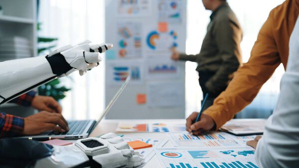 A modern office scene depicting a robot hand assisting professionals with data analysis and strategic planning, highlighting innovation and collaboration.Noogenesis