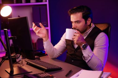 Gülümseyen zeki işadamı, elinde kahve fincanı olan satış ekibiyle buluşuyor ve geceleri Mor Neon Light Home Office 'deki bilgisayar ekranında ürün hedef pazarını araştırıyor. Tahmin et..