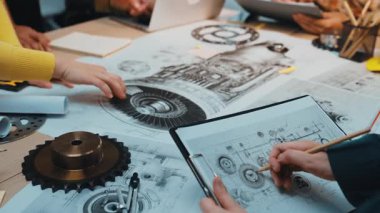 Bir grup profesyonel masa etrafında işbirliği yaparak, ayrıntılı planlar ve mühendislik projeleri ve yenilikler için mekanik bileşenleri analiz ederken tartışmalara da katılıyor. SACTR