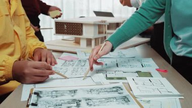 Çeşitli bir grup modern bir ofis içinde takım çalışması yapıyor, yaratıcı proje fikirleri üzerinde işbirliği yaparken ayrıntılı mimari planlar ve modelleri analiz ediyor, yenilikçi çözümler keşfediyor. SACTR