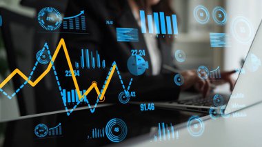 Bir iş adamı, yenilikçi grafikler ve grafiklerle çevrili bir laptopta veri görselleştirmesi yapar ve dinamik ofis ortamındaki anahtar istatistikleri ve eğilimleri vurgular. Xenic