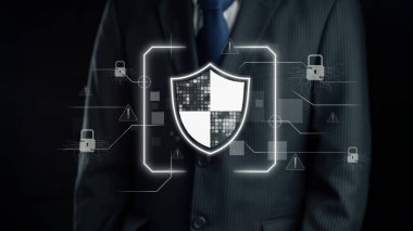 Zarif takım elbiseli bir işadamı, temel siber güvenlik tedbirleri ve modern veri koruma stratejilerini sembolize eden dijital bir kalkan sergileyerek karanlık bir zemine karşı duruyor. Dörtgen