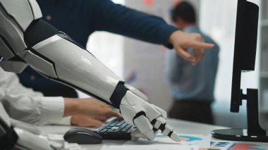 İnsan meslektaşları tartışırken, gelecekçi bir robot kolu bilgisayara doğru uzanıyor. Bu sahnede modern ofis ortamlarında takım çalışması, teknoloji ve yenilik vurgulanıyor. Noogenesis