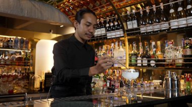 Asyalı barmen karışık kremalı votka bardağı servis ediyor. Önünde buzlu pembe çiçekli şeker, önünde özel içecek, lüks tezgah barında alkolü canlandırıyor. Vinosity.