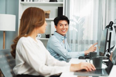 Gülümseyen Asyalı bir adam, yan görüntüdeki modern ofis çalışma masasında veri tabanını ararken günlük dizüstü bilgisayarla pazarlama raporu projesini planlarken kadın meslektaşıyla konuşuyor. İnfobahn.