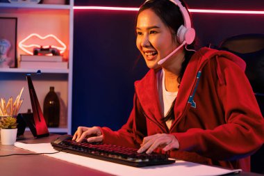 İnternet üzerinden kulaklık takıp gülümseyen Asyalı güzel kız flamasının sunucu kanalı izleyicilerle internet üzerinden konuşma yapıyor. Esport yetenekli takım oyuncuları neon mavi odada. Taktik.